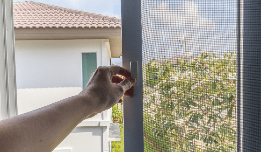 Egy kéz egy ablakot nyit, ahol a szúnyogháló előtt virágzó cserjére látható kilátás nyílik.